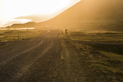 Dirt road amidst field during sunset