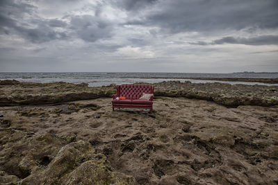 Abandoned sofa at beach against sky