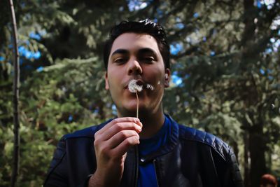 Portrait of young man blowing dandelion seeds