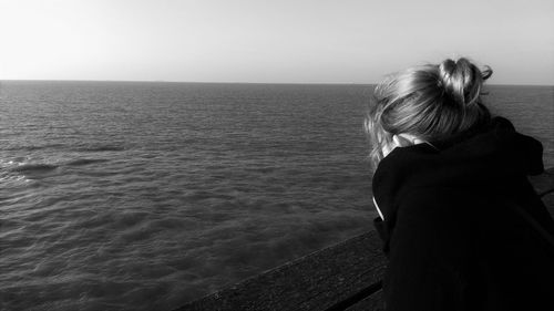 Rear view of woman standing by sea against clear sky