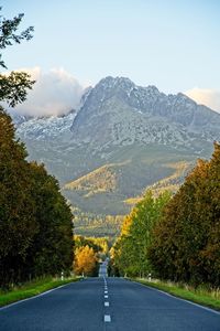 Empty road along trees and mountains against sky