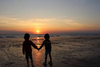 Silhouette people on beach against sky during sunset