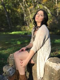 Portrait of young woman sitting on rock at park