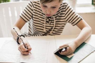 High angle view of boy using mobile phone while studying at table in house