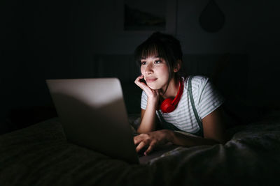 Young woman using mobile phone while sitting on bed at home