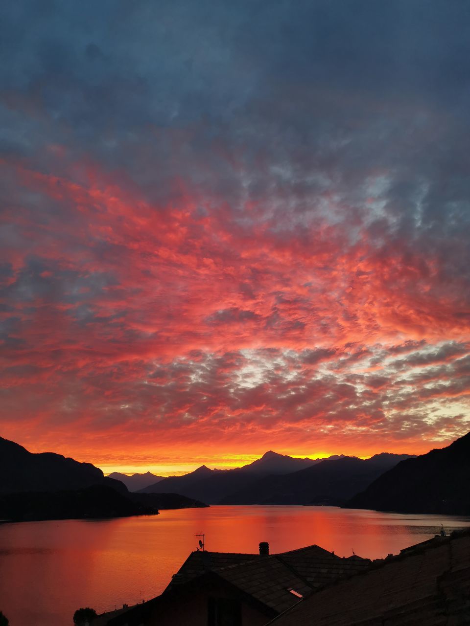 sky, mountain, cloud, afterglow, sunset, beauty in nature, water, scenics - nature, red sky at morning, nature, dawn, architecture, mountain range, dramatic sky, no people, tranquility, silhouette, evening, landscape, orange color, environment, tranquil scene, built structure, horizon, sea, outdoors, building, building exterior, red, travel destinations, house, idyllic, reflection, romantic sky, land