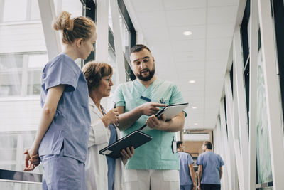 Male healthcare worker explaining over clipboard to doctor at hospital