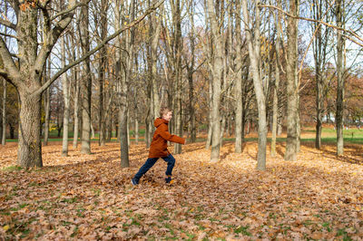 A cute boy in a jacket runs through an autumn yellow park among the trees