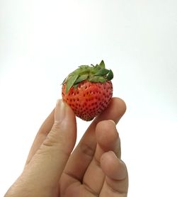 Close-up of hand holding strawberry over white background