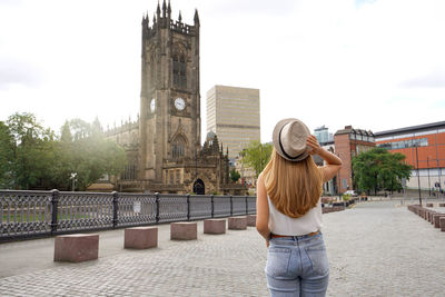 Back view of beautiful blonde girl walking in manchester city on sunny day, england, united kingdom