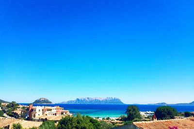 Distant view of town by sea against clear blue sky