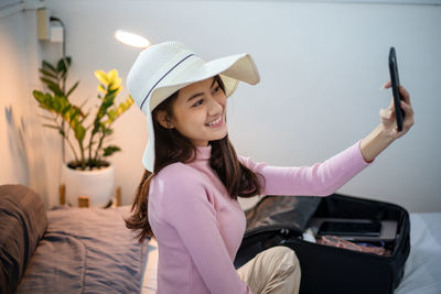 Young woman using mobile phone while sitting on bed at home