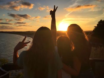 Silhouette people at shore against sky during sunset