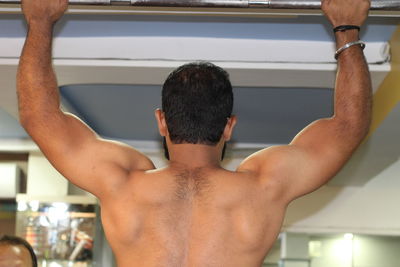 Rear view of shirtless man exercising at gym