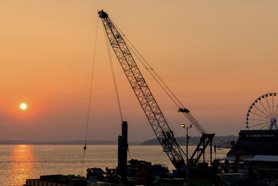 Silhouette crane at harbor against orange sky