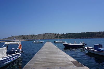 Sailboats moored in sea against clear blue sky