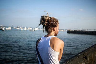 Rear view of man sitting on retaining wall at beach against sky