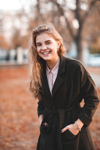 Smiling young woman standing with hands in pockets