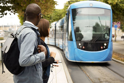Commuters waiting on sidewalk while looking at blue tram in city