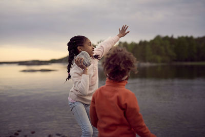 Girl throwing rock while standing by brother at beach during sunset