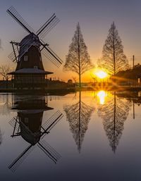 Traditional windmill by lake against sky during sunset