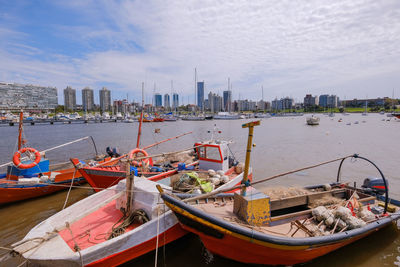 Fishing boats moored on sea by buildings against sky