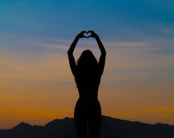 Silhouette woman with arms raised against sky during sunset