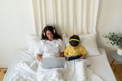 Mom typing on laptop computer lying in bed with preschool son kid watch video or cartoon on tablet