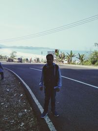 Full length portrait of man standing on road against sky