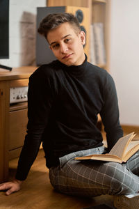 Portrait of man with book sitting on floor at home