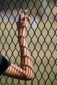 Close-up of hand on chainlink fence against sky