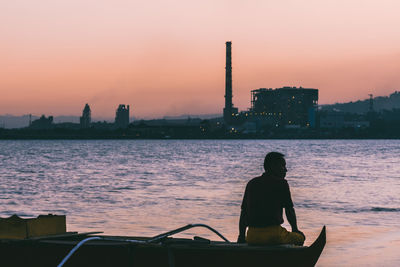 Rear view of man sitting on boat against sky during sunset