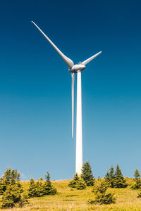 Low angle view of wind turbines on field against clear blue sky