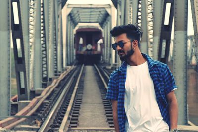 Young man wearing sunglasses standing on railway bridge