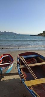 Boats moored on beach against clear sky