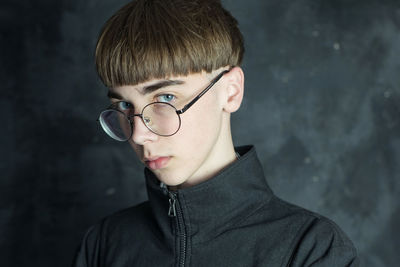 Portrait of young man wearing eyeglasses against wall
