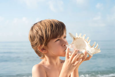 Close-up of shirtless boy holding seashell at beach