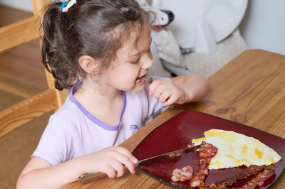 Young girl eating eggs and bacon with knife and fork for the first time