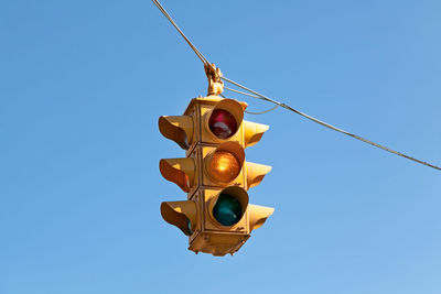 A 4 directions traffic light / stoplight hanging from a cable with blue sky behind