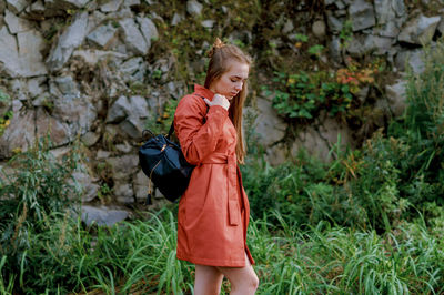 Portrait of young woman holding bag while standing on grassy field