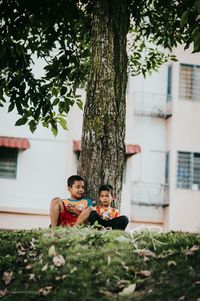 Surface level of boys sitting by tree trunk on field