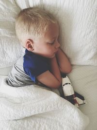 High angle view of cute boy sleeping with airplane toy on bed