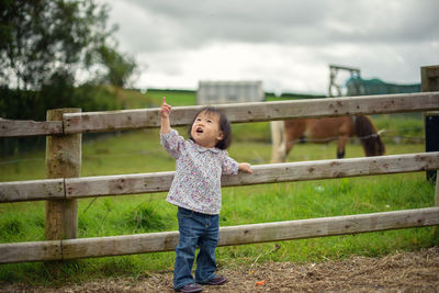 Baby boy looking up while standing by wooden fence at barn