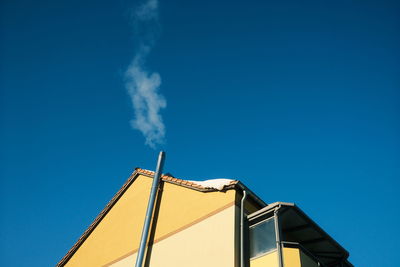 Low angle view of smoke emitting from chimney against clear blue sky