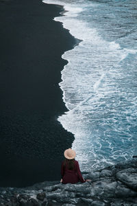 Rear view of woman sitting on rock at beach