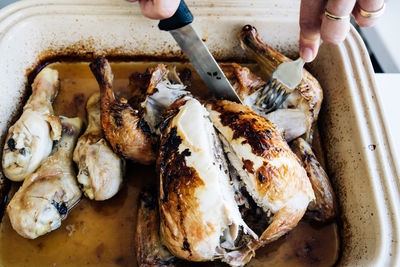 Cropped hands cutting roast chicken in container