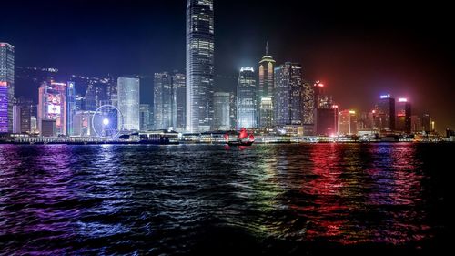 Illuminated cityscape at harbor against sky at night