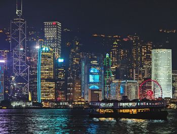 Illuminated buildings by river against sky in city at night