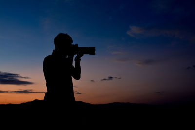 Silhouette man photographing against sky during sunset