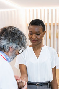 Focused senior male doctor measuring pulse of black female patient during check up in hospital